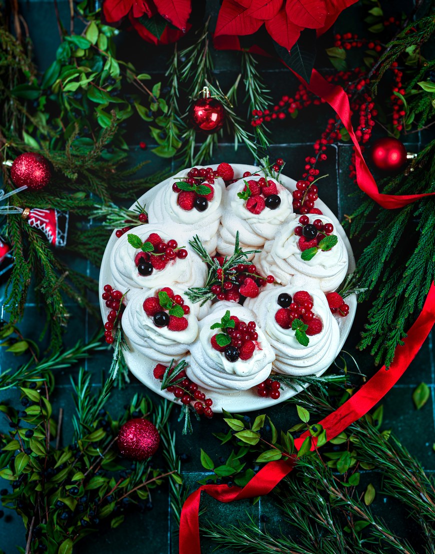Pavlova Tricolore, Baiser-Kranz mit Ricotta-Creme, Himbeeren, Johannisbeeren und Rosmarin zwischen Tannengrün und Weihnachtskugeln