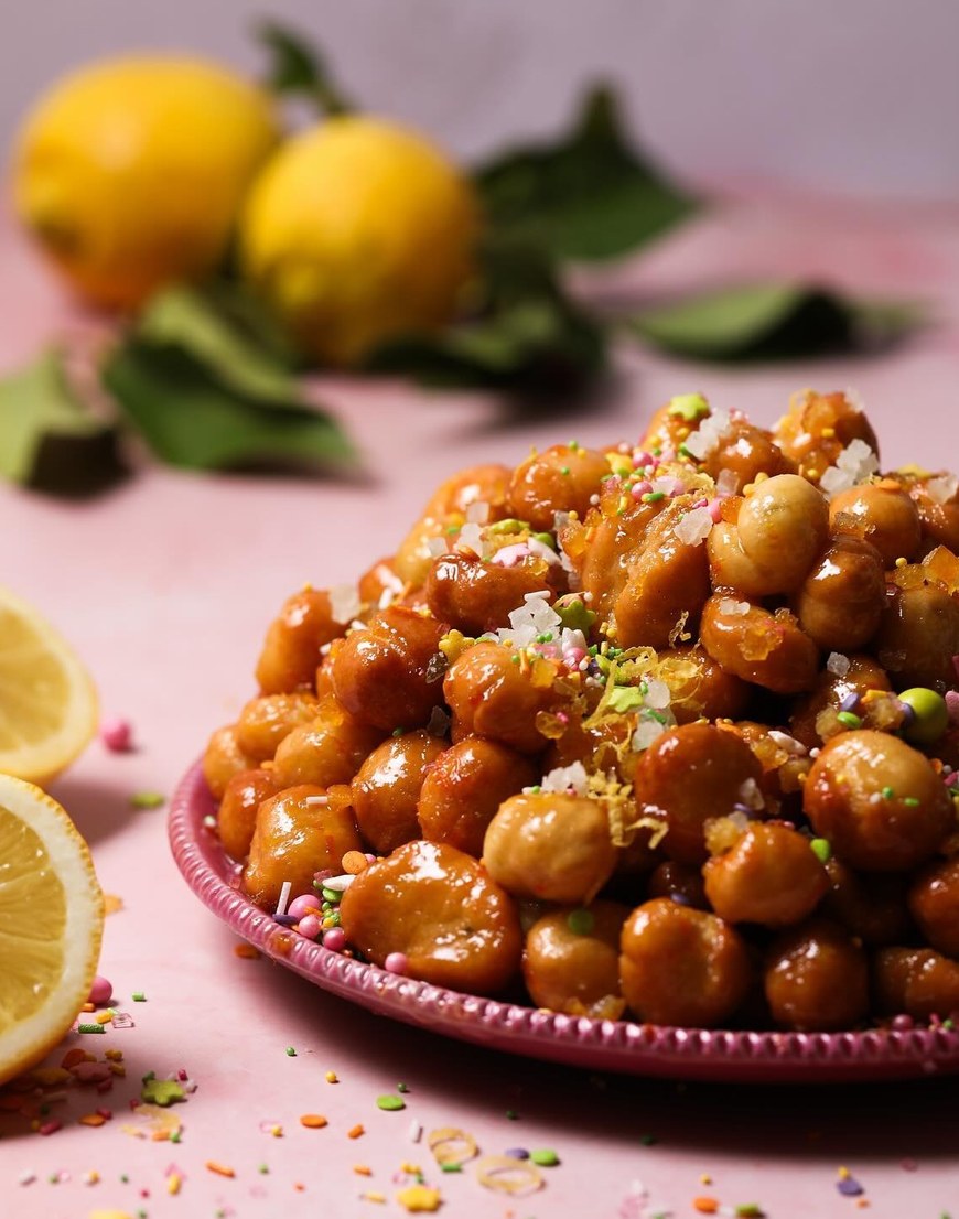 Struffoli alla Napoletana, kleine Teigkugeln in Honig mit Zitronenabrieb und bunten Zuckerstreuseln auf rosa Teller